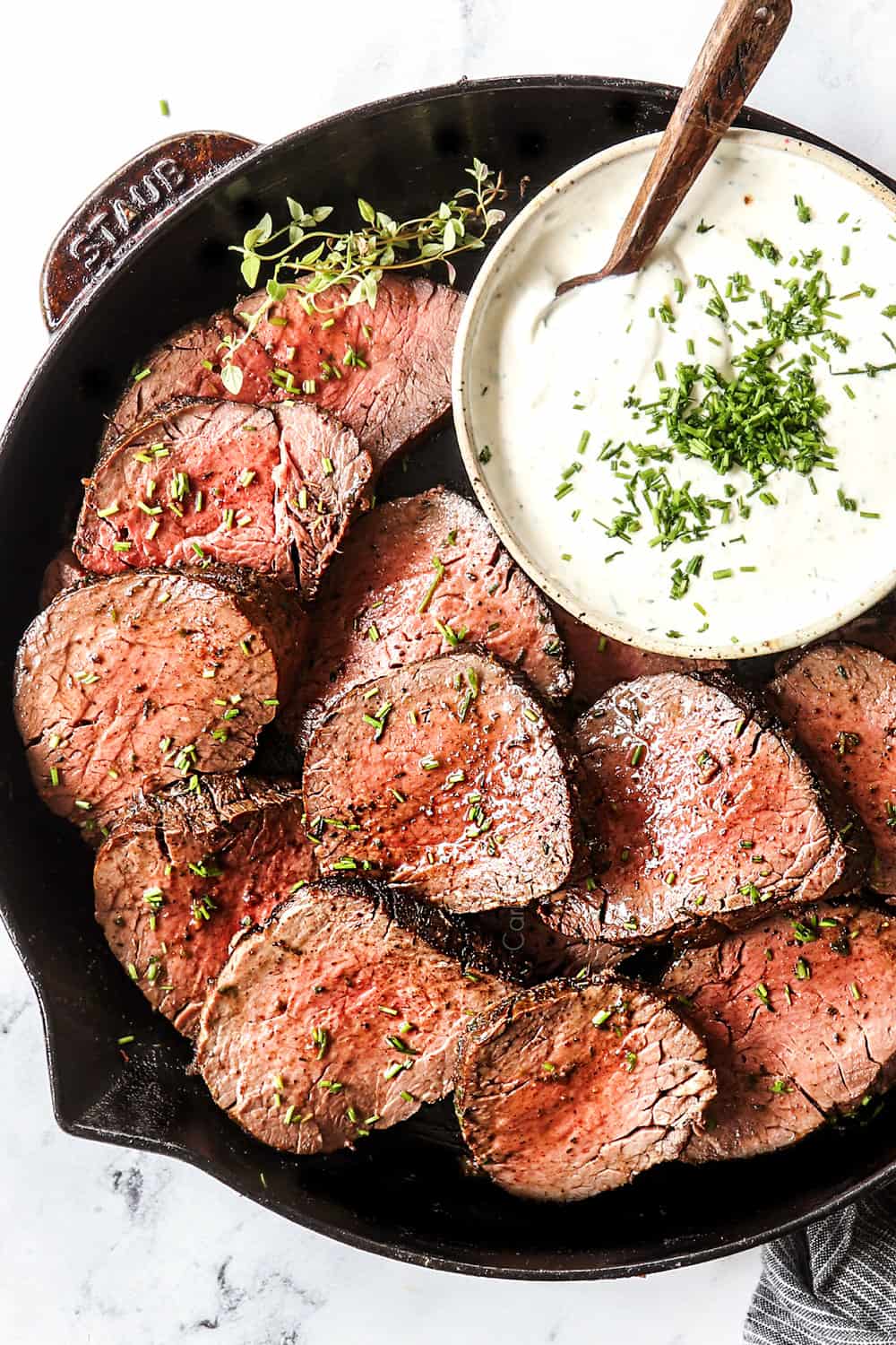 showing how to serve horseradish cream sauce by plating it with sliced beef tenderloin in a skillet