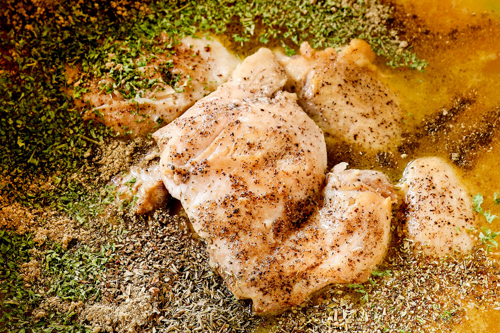 showing how to make chicken pot pie soup recipe by adding chicken, spices and seasoning to the pot with the vegetables