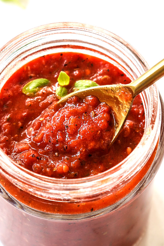 homemade pizza sauce in a glass jar with a gold spoon showing the chunky texture