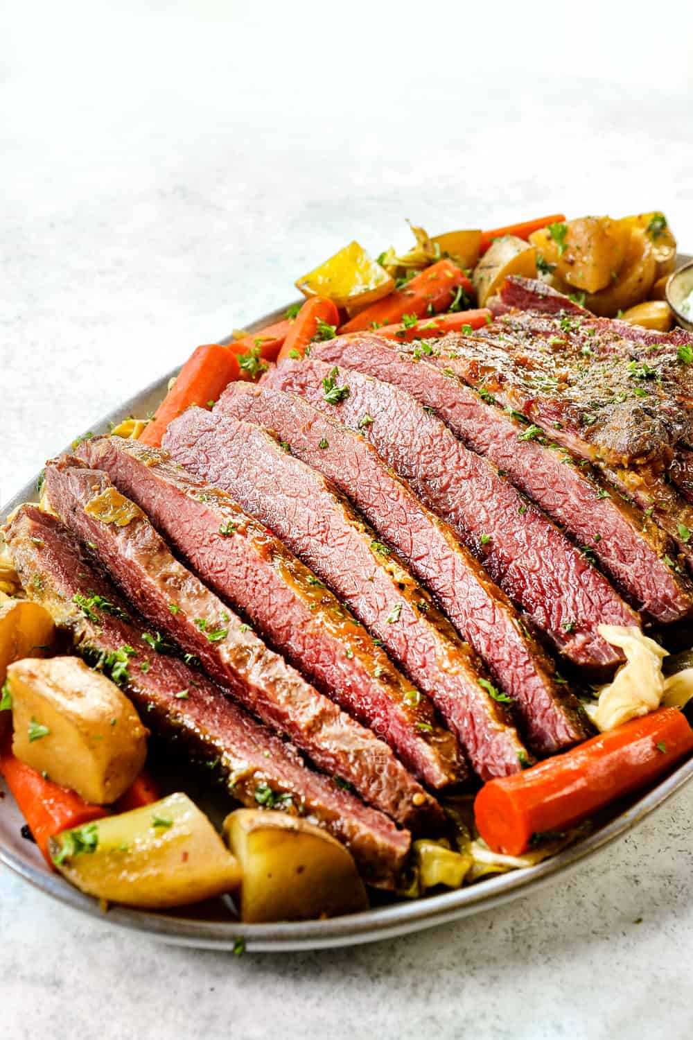side view of corned beef and cabbage on a platter with potatoes, carrots and horseradish sauce