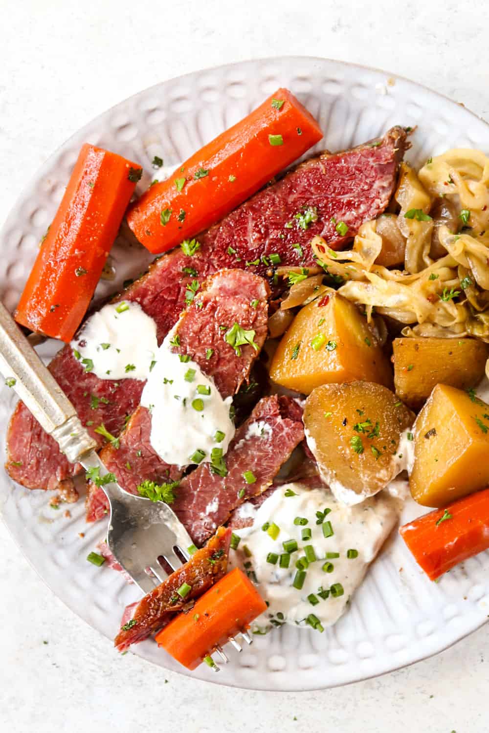 top view of corned beef brisket sliced on a white plate with cabbage, potatoes and carrots