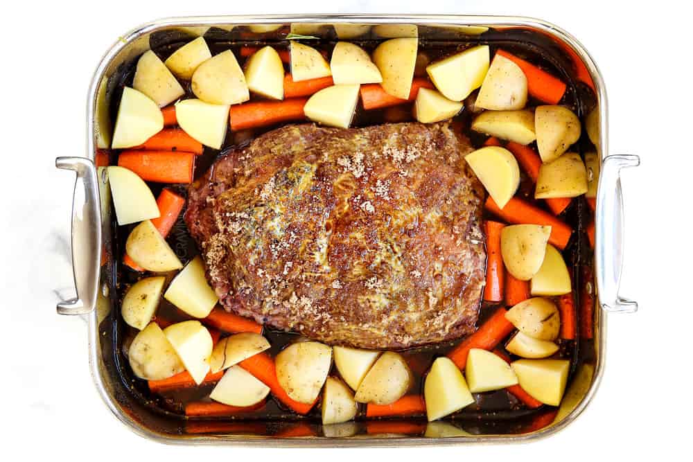 showing how to cook corned beef by adding brisket to a roasting and surrounding with carrots and potatoes