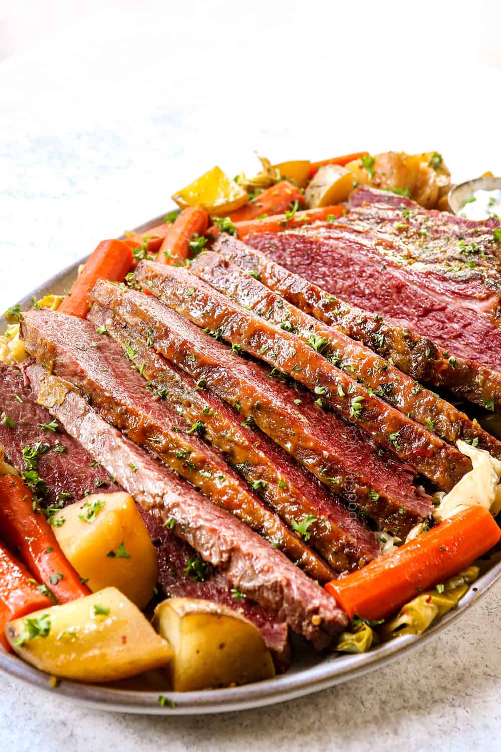 side view of corned beef and cabbage on a platter with potatoes, carrots and horseradish sauce