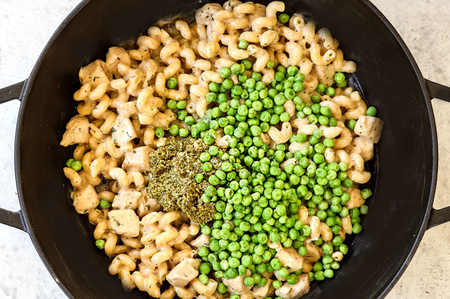 showing how to make chicken pesto pasta recipe by stirring in pesto, peas and Parmesan into the cooked pasta