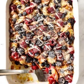top view of sweet breakfast casserole with croissants, berries and lemon drizzle in a white casserole dish