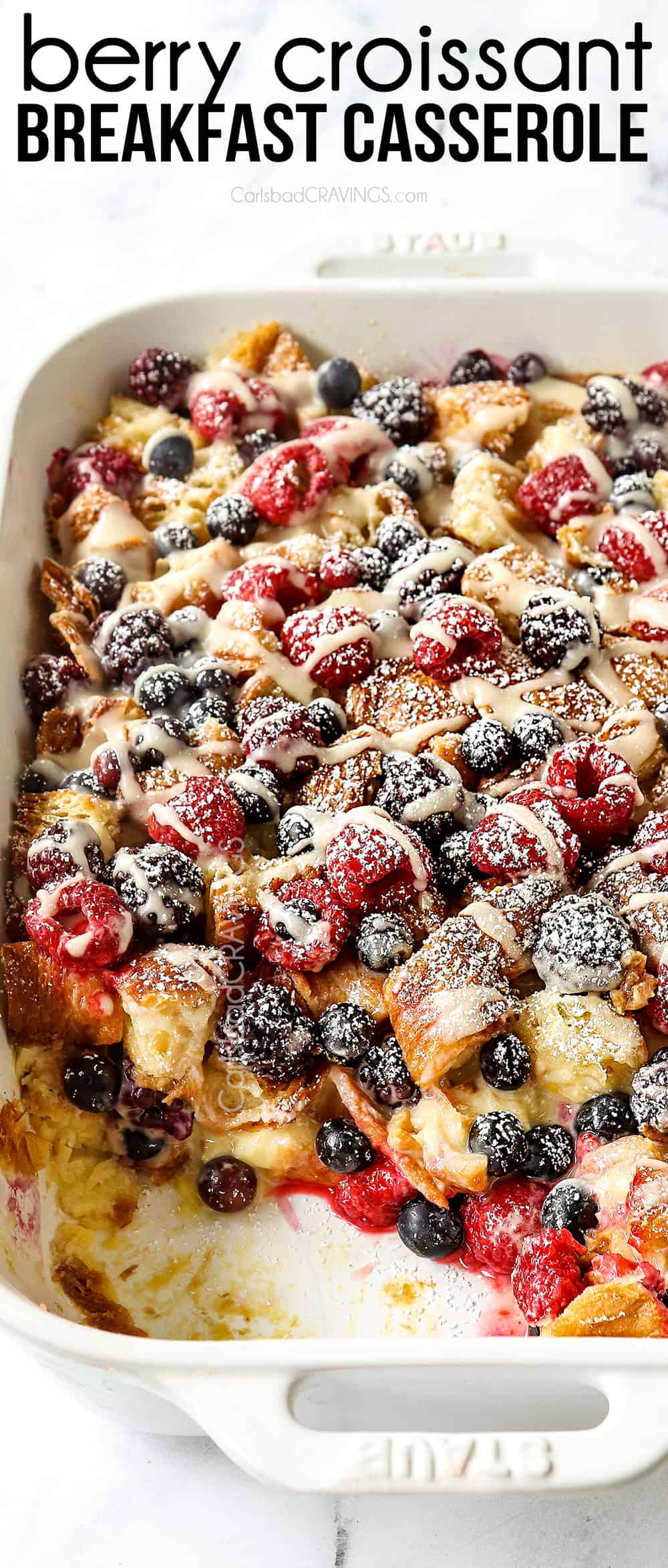 top view of sweet breakfast casserole with croissants, berries and lemon drizzle in a white casserole dish