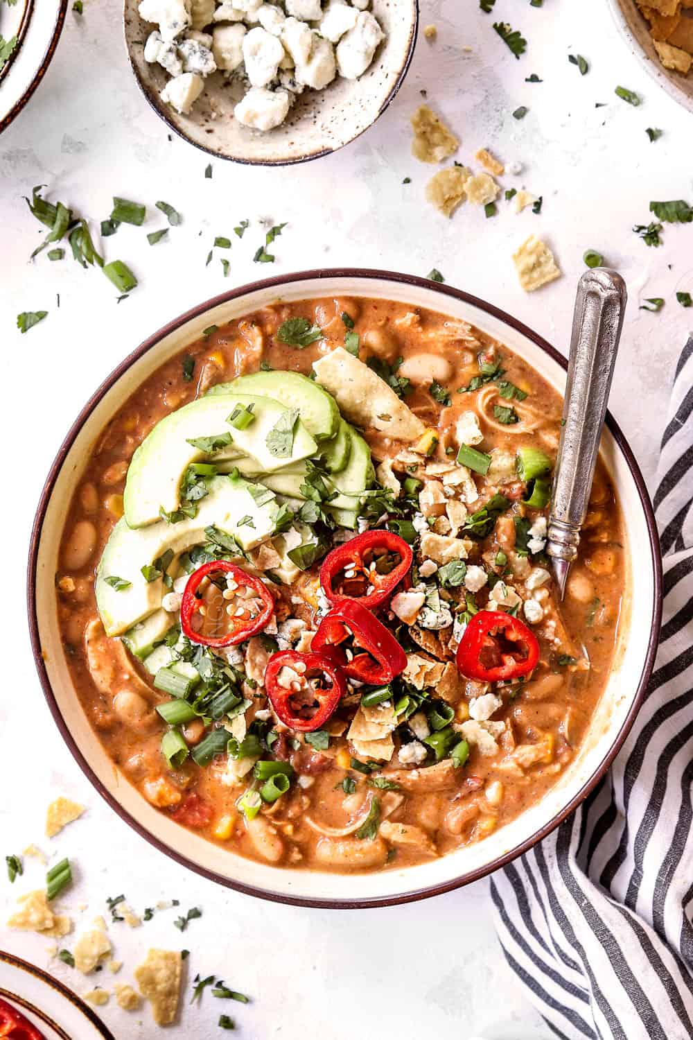 showing how to top a bowl of buffalo chicken chili by adding chips, blue cheese and avocados