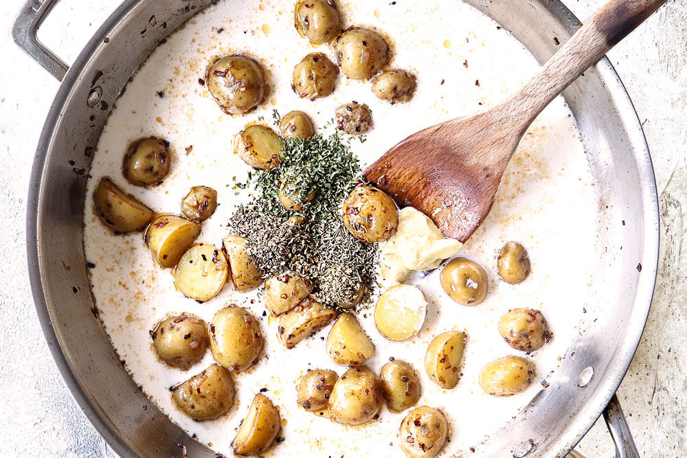 showing how to make creamy Chicken mushroom recipe by adding potatoes, seasonings and heavy cream to skillet to make creamy mushroom sauce