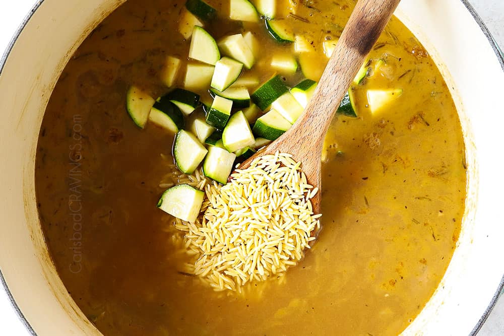 showing how to make lemon chicken orzo soup by adding orzo and zucchini to the soup