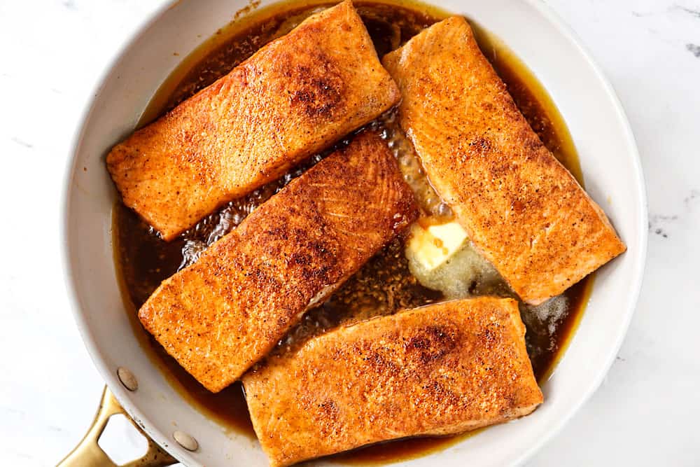 showing how to make honey glazed salmon recipe by adding honey garlic sauce to the middle of the skillet along with butter