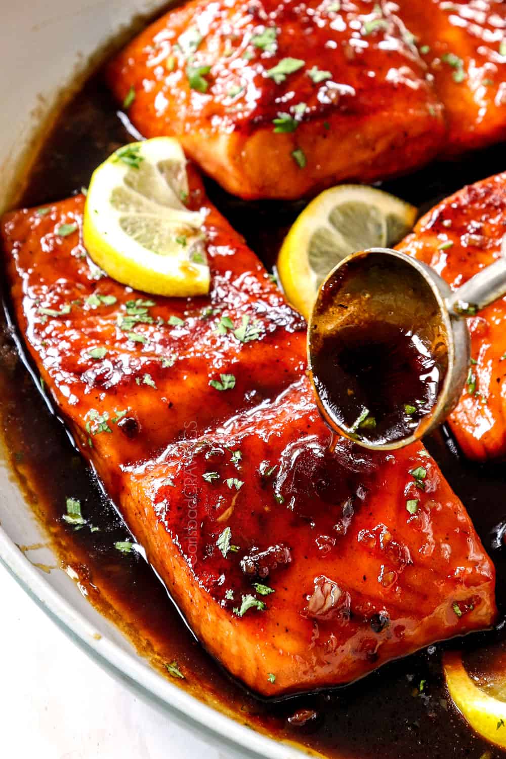 showing how to make honey garlic glazed salmon by drizzling salmon with honey garlic sauce while simmering in the skillet