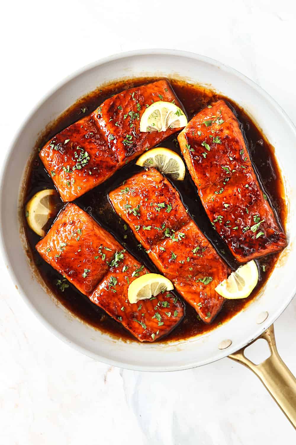 top view of honey garlic glazed salmon in a white skillet garnished by parsley