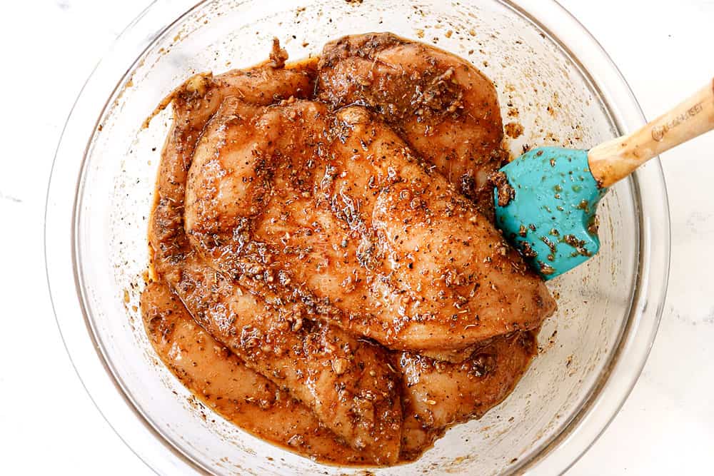 showing how to make Greek chicken by coating chicken breasts in Greek chicken marinade