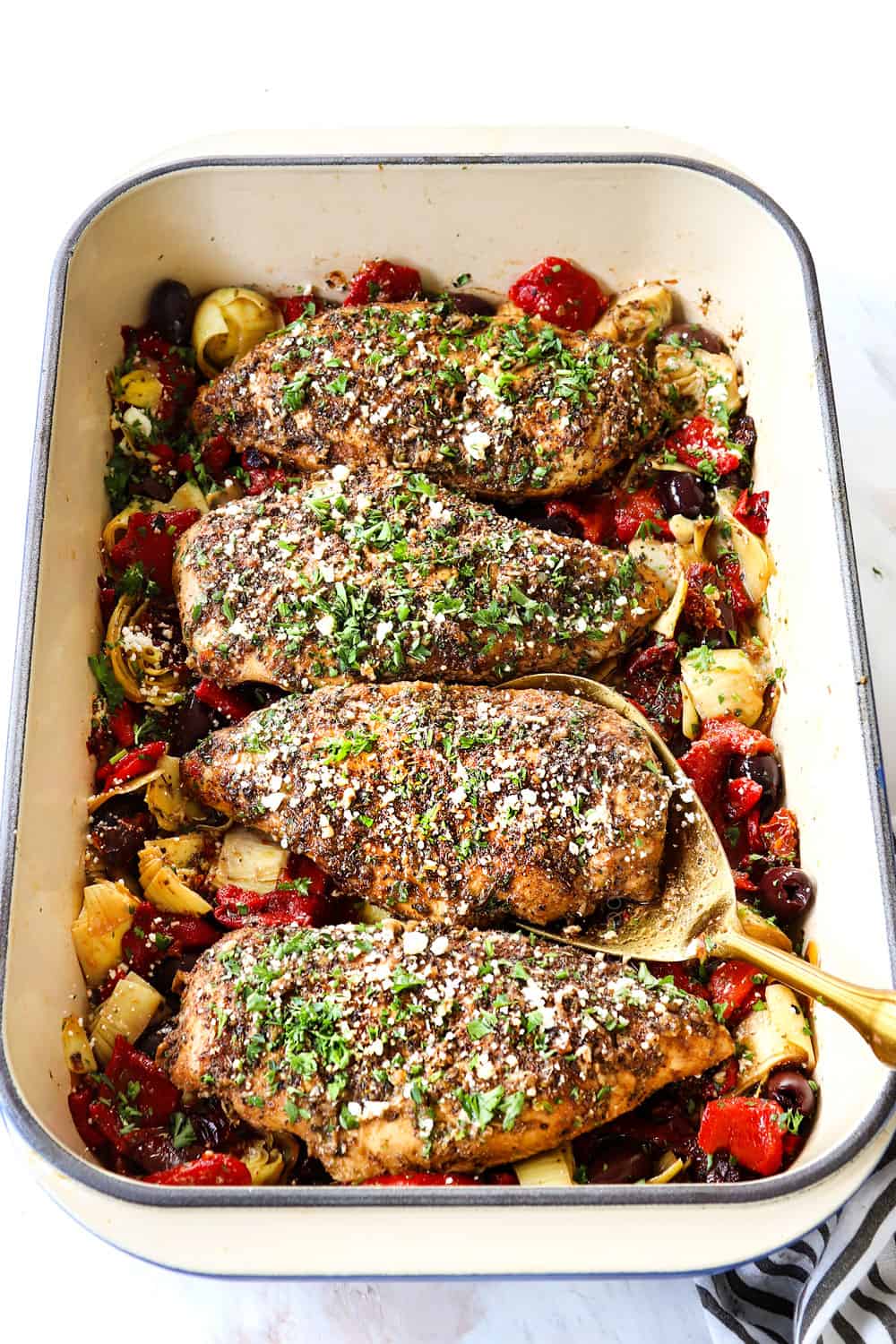 serving Greek chicken by scooping up a piece of chicken with a golden spoon