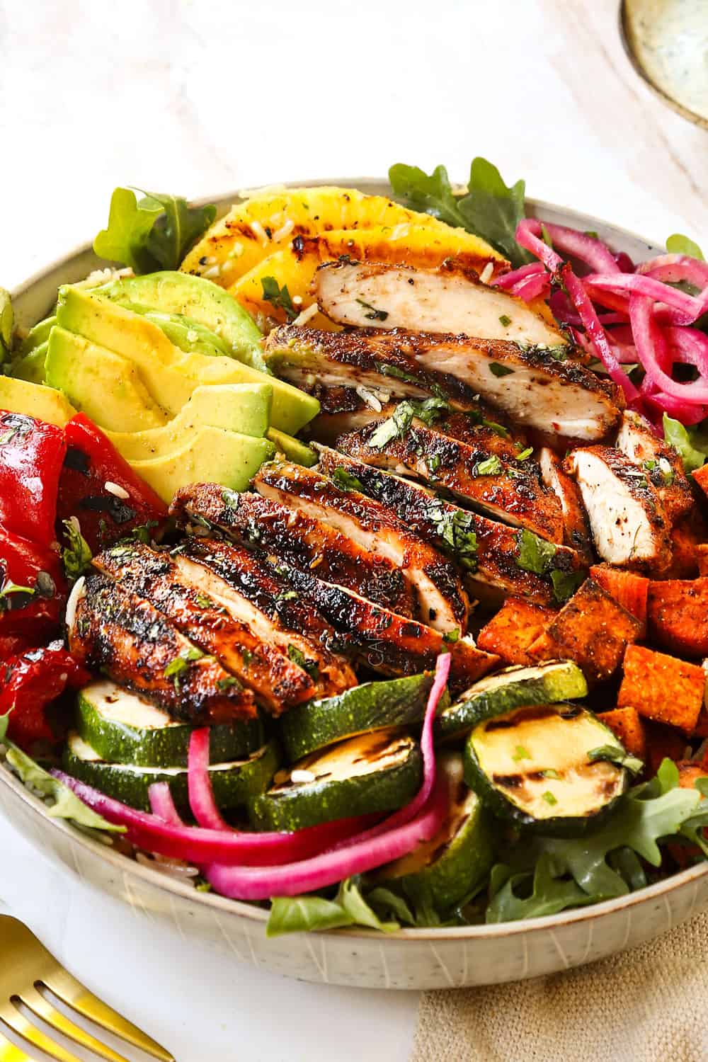 side view of serving harissa chicken thighs in a bowl with bell peppers, sweet potatoes and pickled red onions showing how to serve the recipe