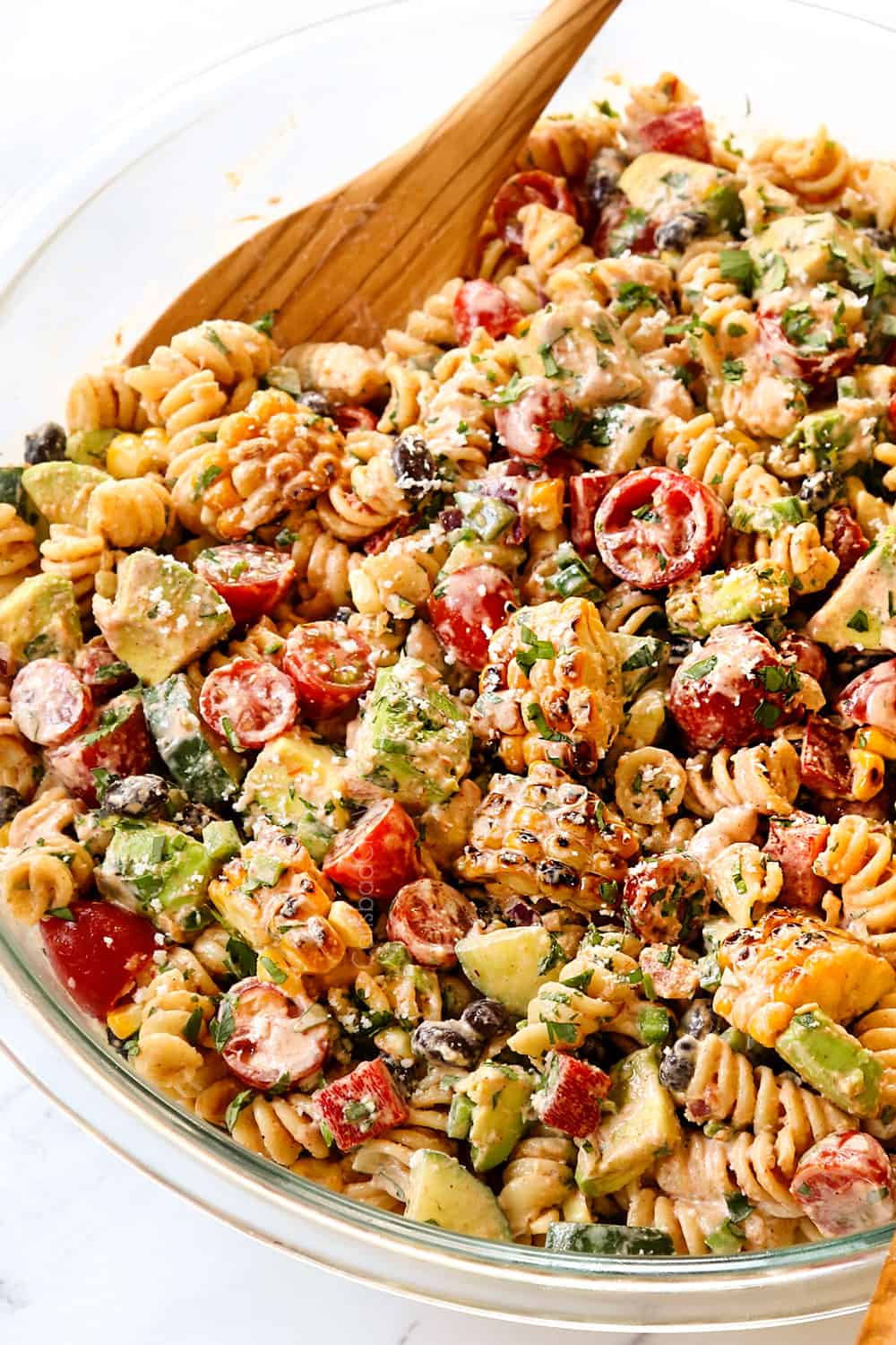Mexican Pasta Salad in a glass bowl with wooden spoons