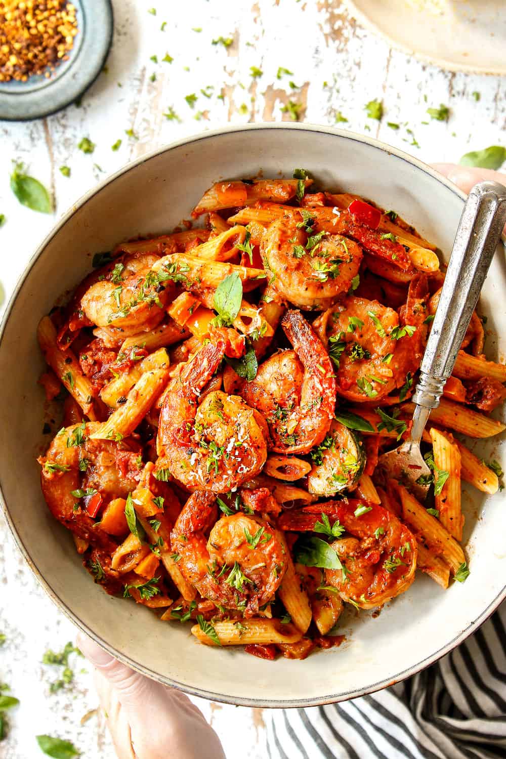 top view of shrimp pasta recipe in a white bowl being held by two hands