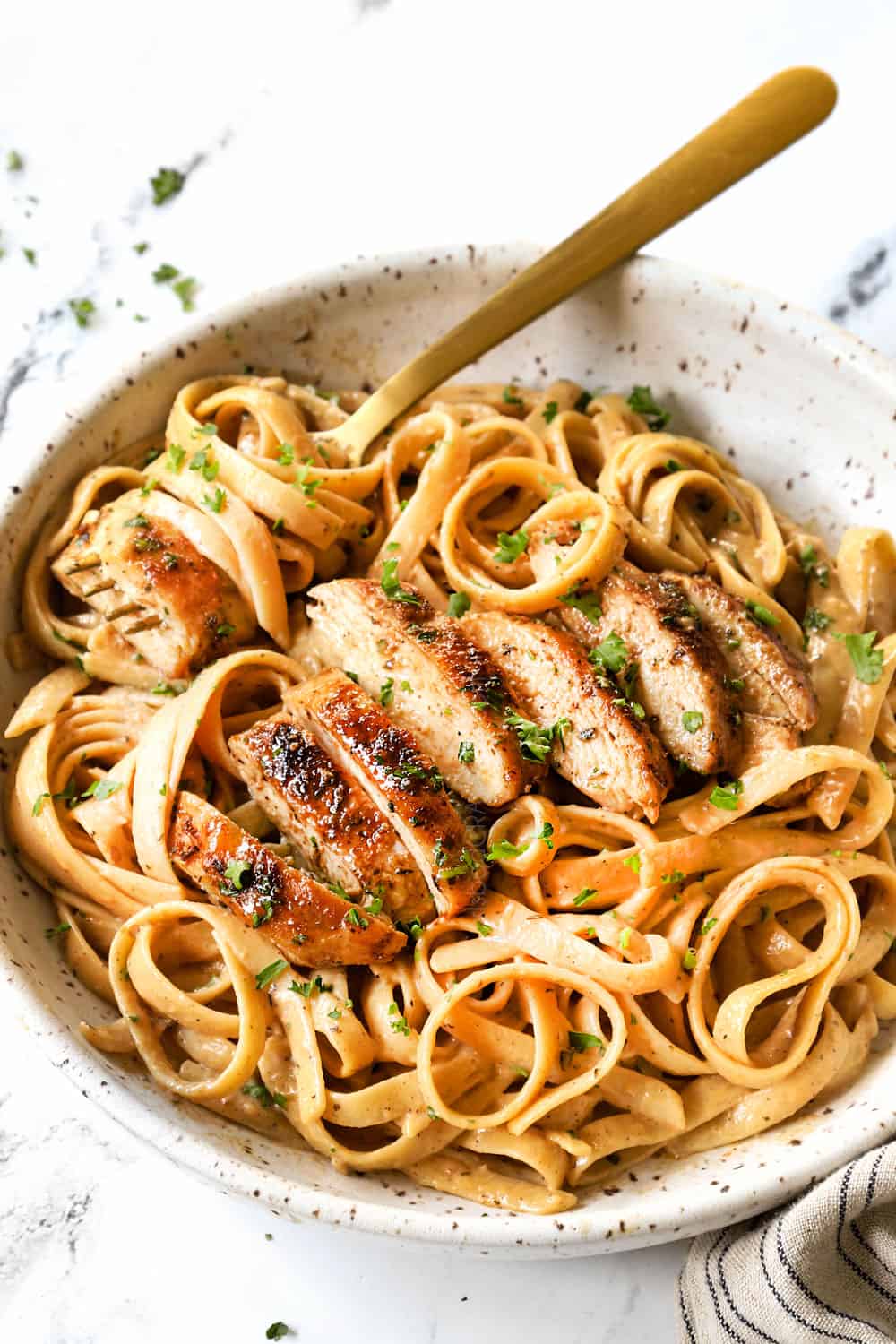 showing how to serve chicken alfredo pasta by slicing chicken and adding to a bowl of fettuccine Alfredo