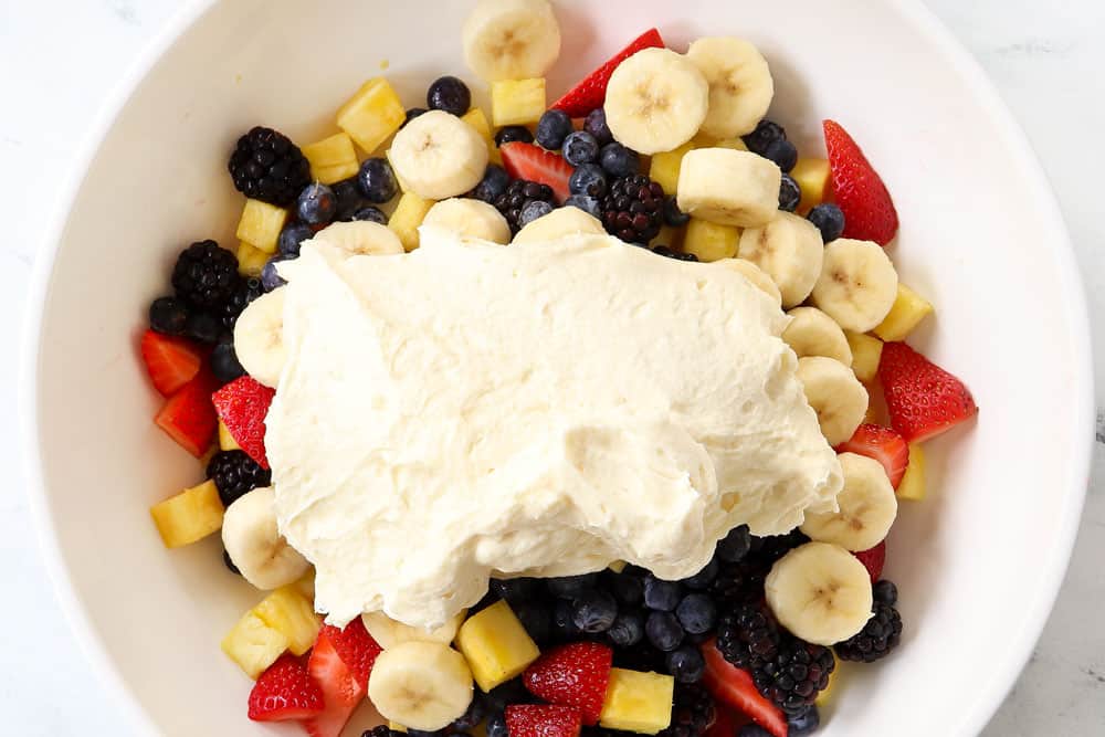 showing how to make cheesecake salad by folding cheesecake filling into strawberries and bananas