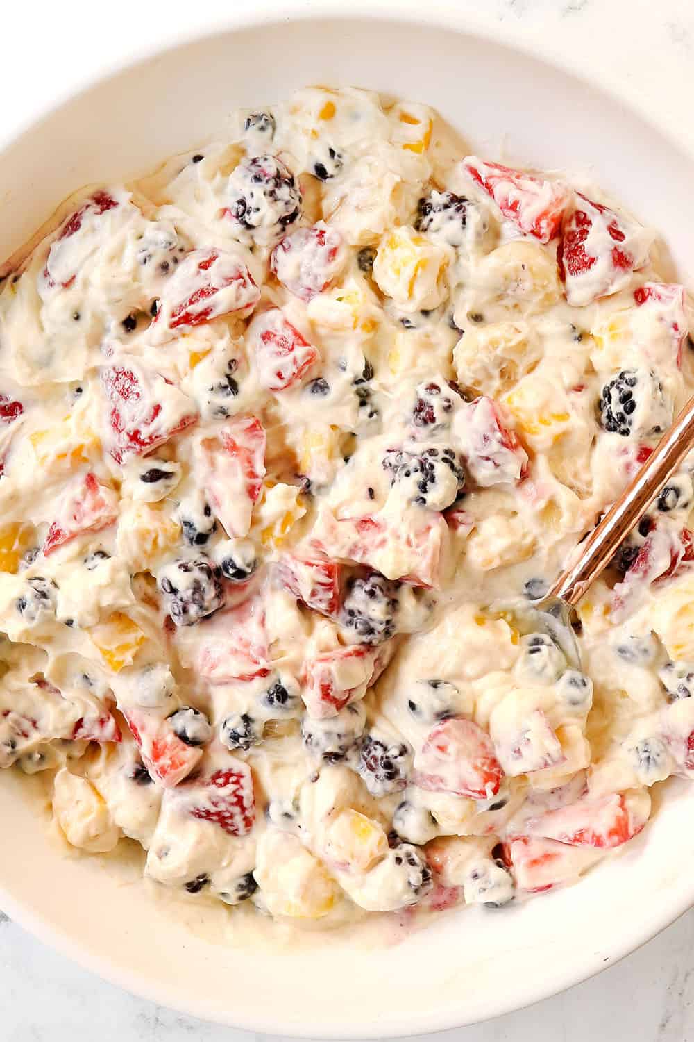 top view of cheesecake fruit salad in a white bowl with strawberries and bananas