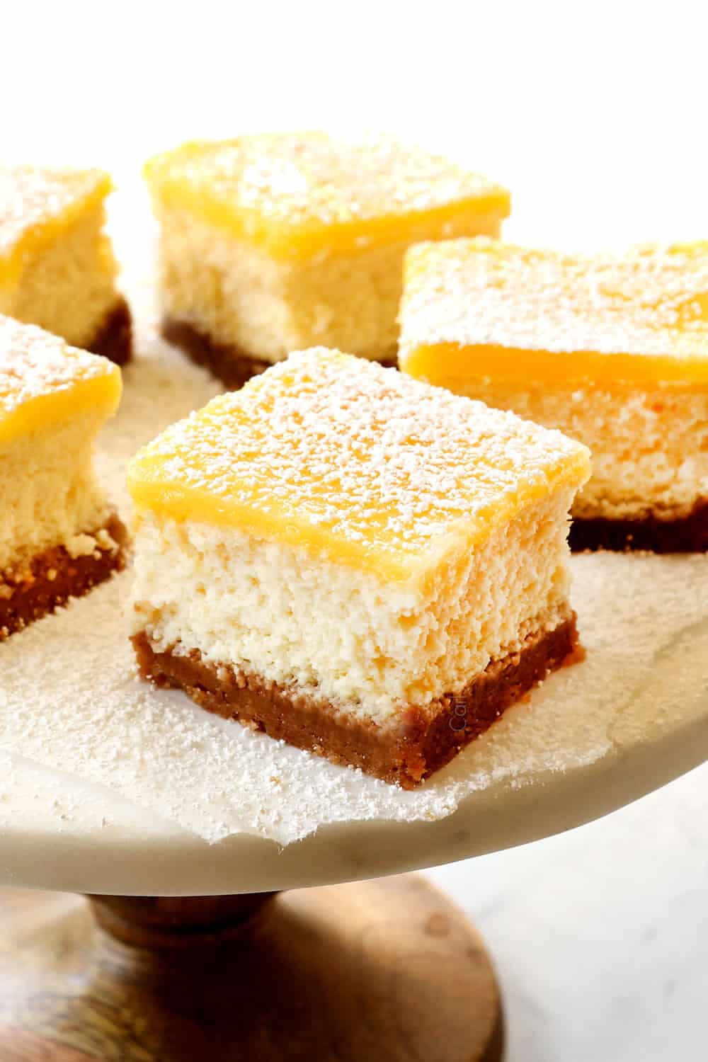 lemon cheesecake bars with lemon curd topping on a cake pedestal
