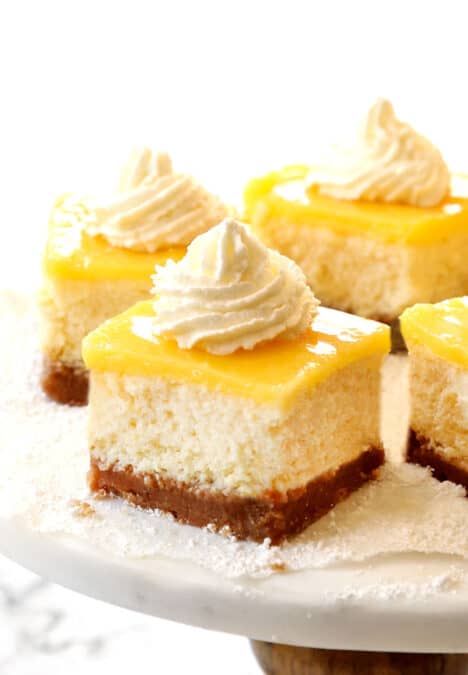 up close of lemon cheesecake bars with whipped cream on a cake pedestal