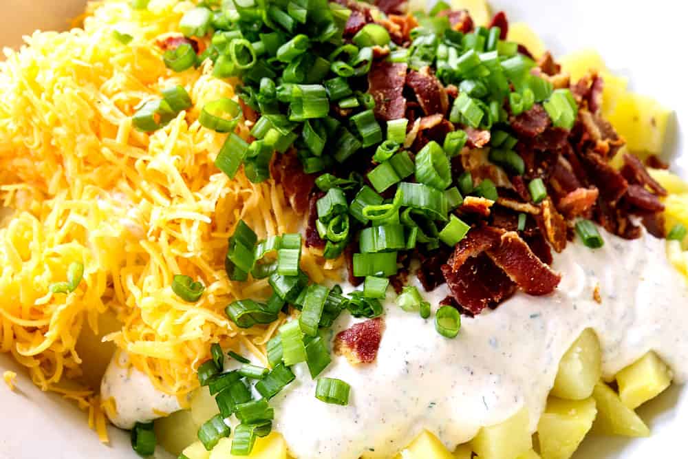 showing how to make potato salad by adding potatoes, cheddar cheese, bacon and chives to a large bowl
