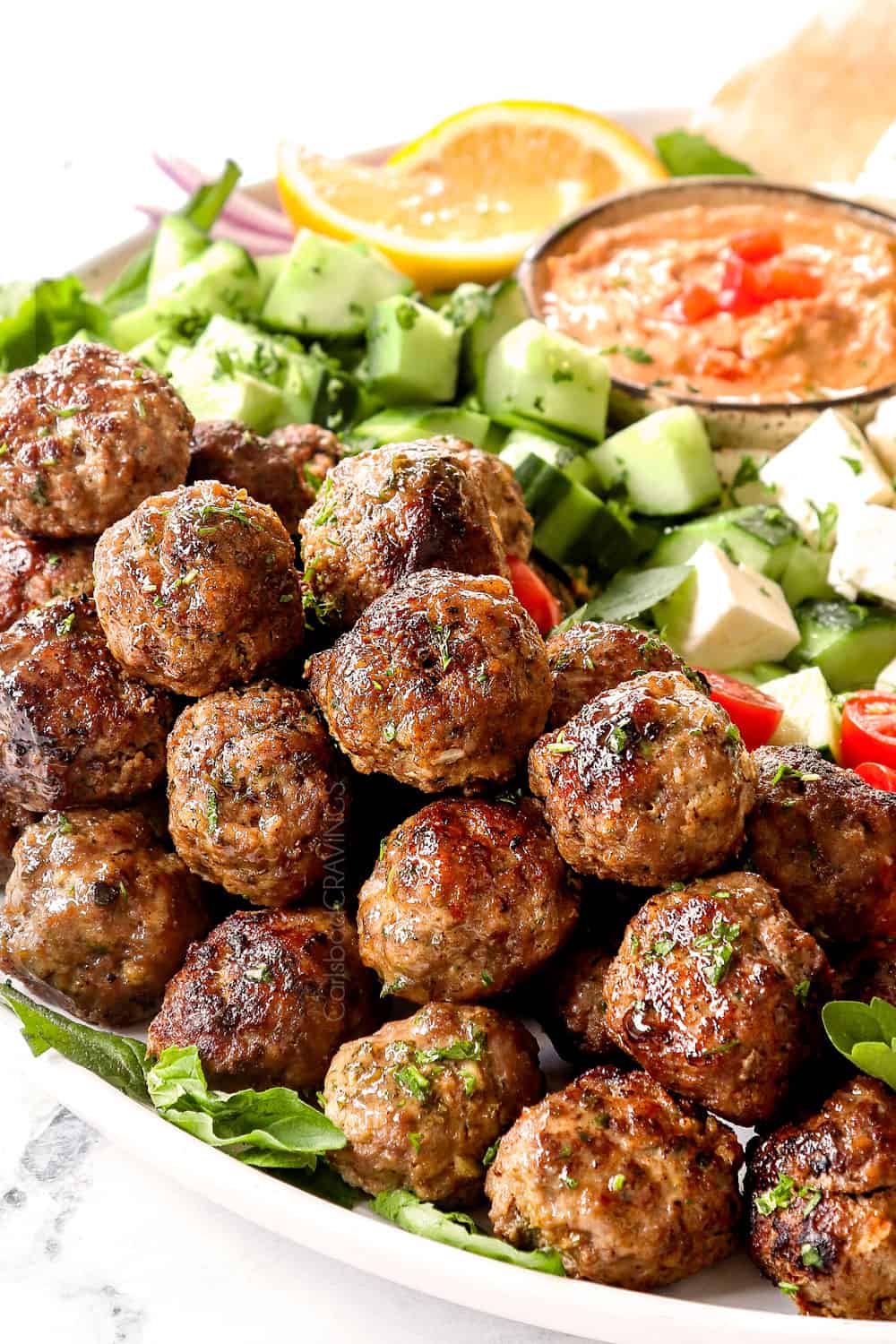 Greek Meatball recipe on a white platter with cucumbers and hummus showing how juicy they are