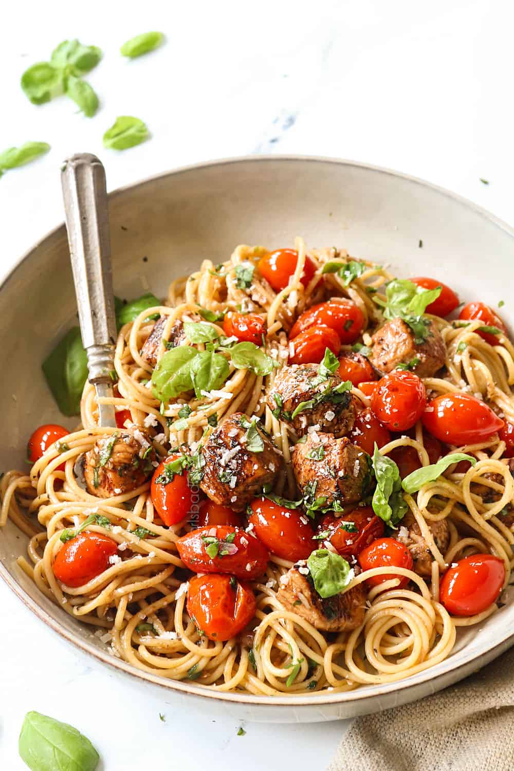 showing how to serve bruschetta chicken pasta recipe by adding to a bowl and garnishing with Parmesan and fresh basil