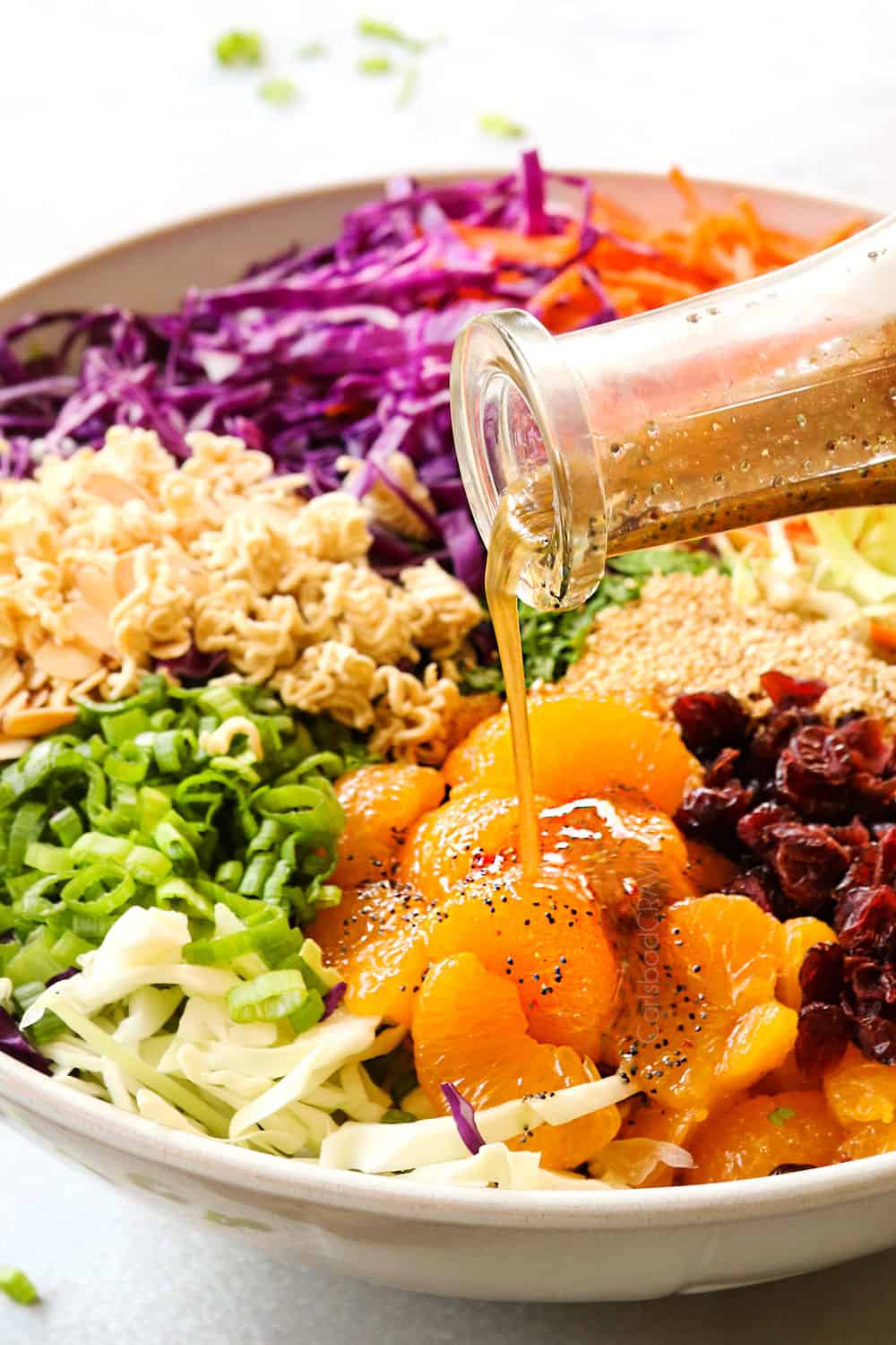 showing how to make Ramen Noodle Salad recipe by pouring salad dressing over the salad