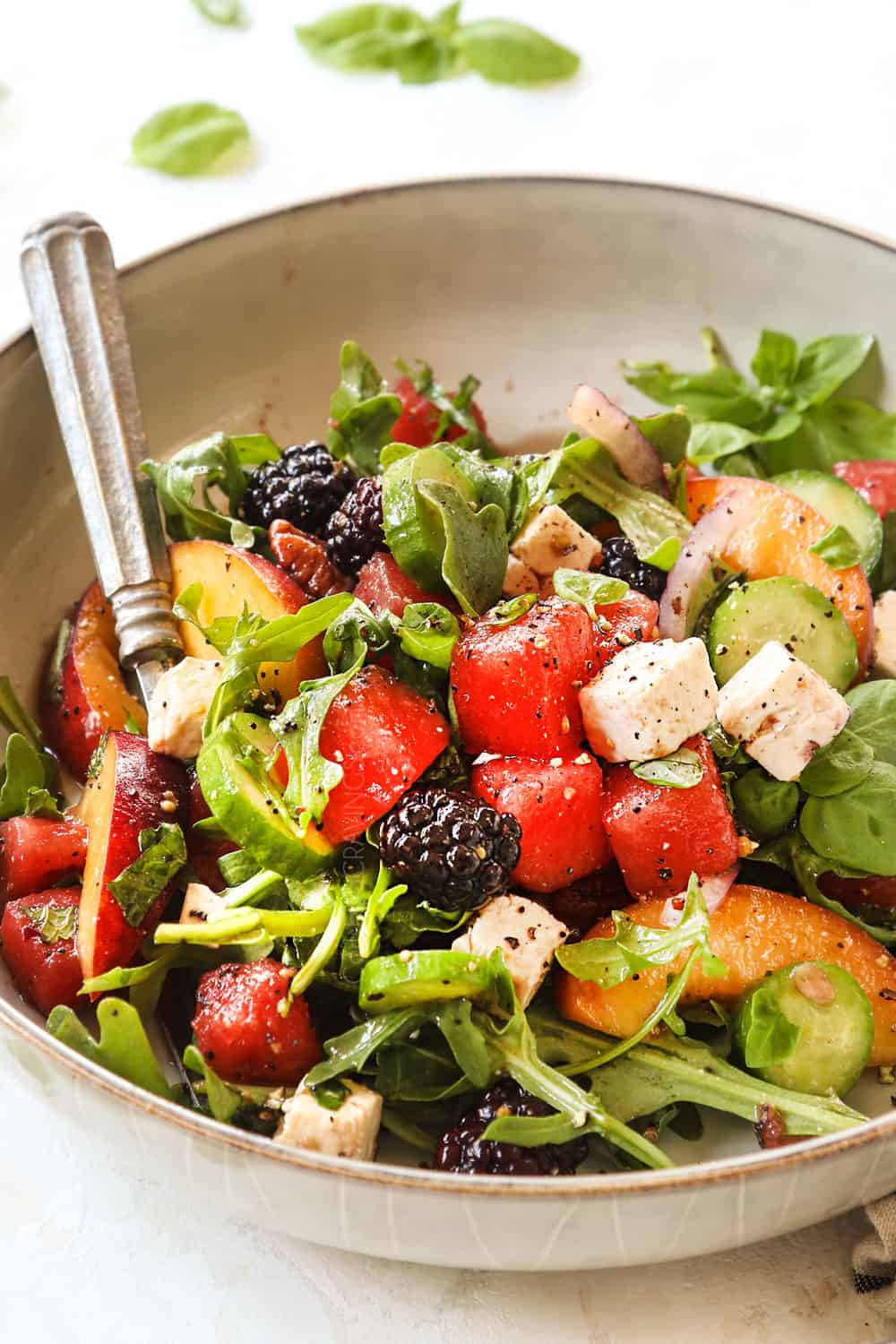a bowl of watermelon salad with feta, mint, basil, cucumbers, and berries over a bed of arugula