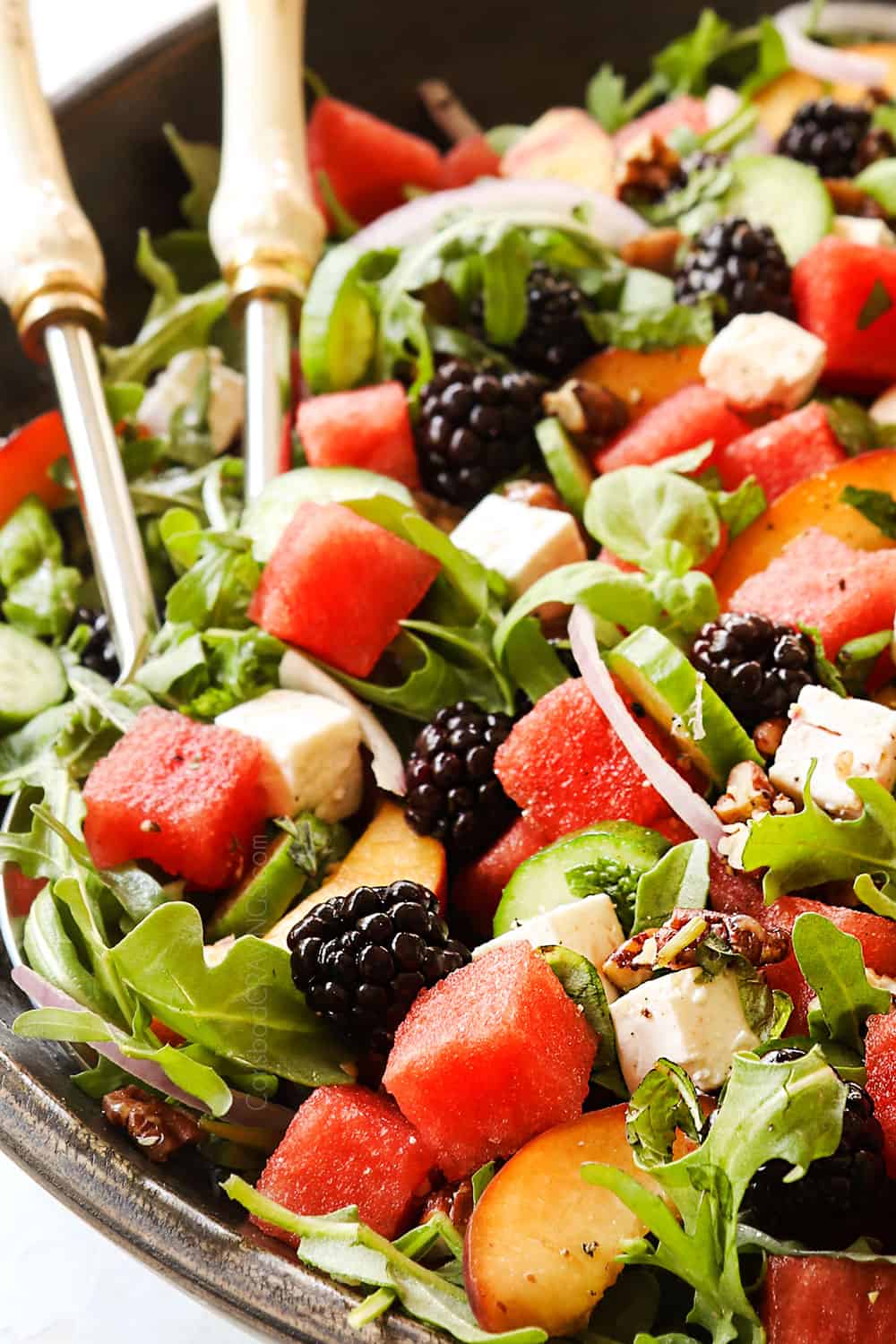 up close of two tongs laying in watermelon cucumber salad