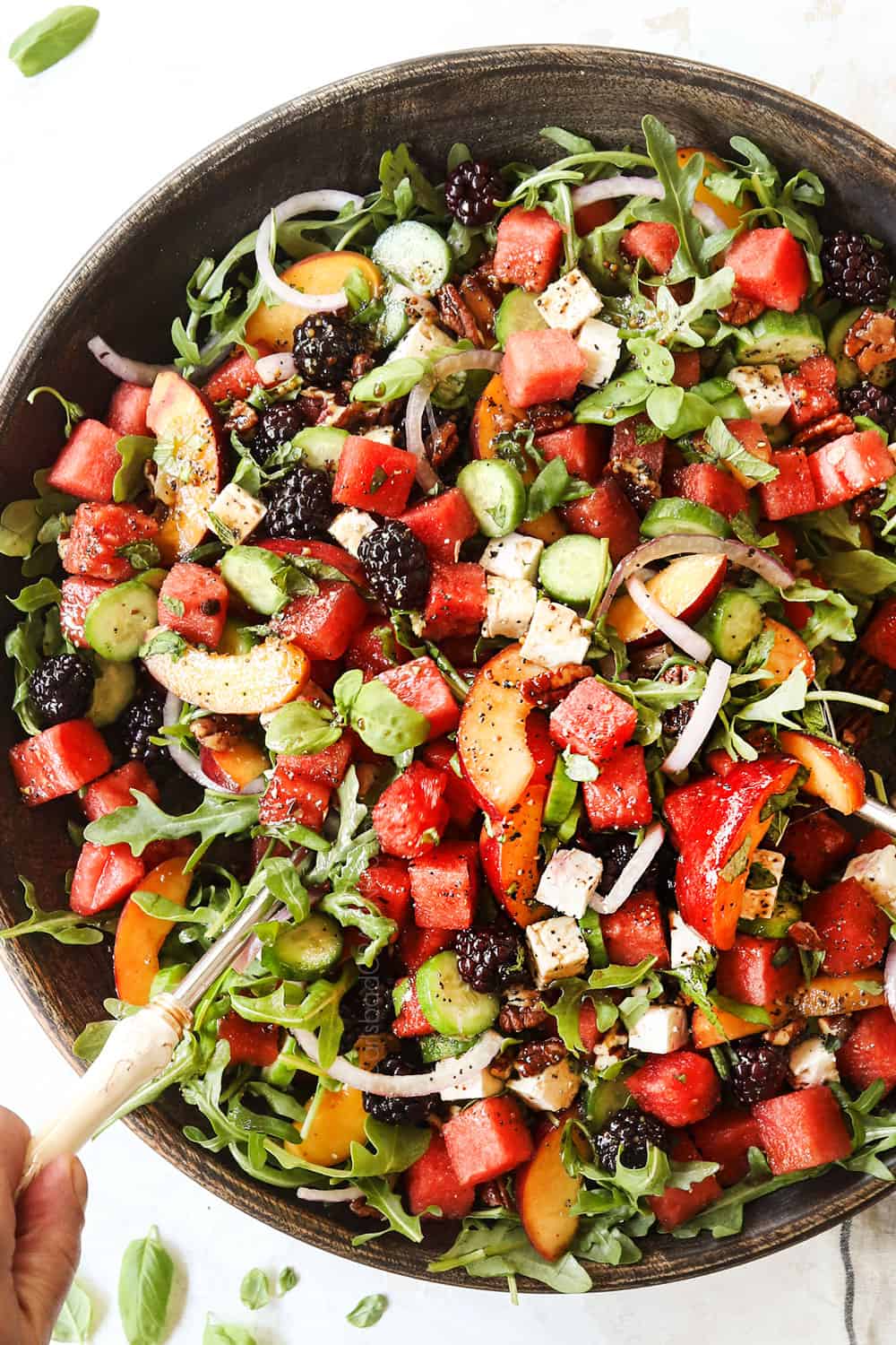 showing how to make watermelon salad recipe by tossing salad together in a large bowl
