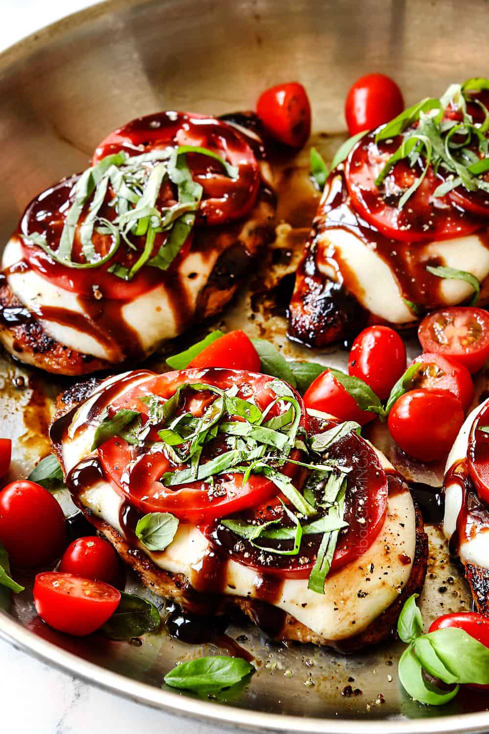 up close showing how to make chicken Caprese by adding basil to chicken on top of the tomatoes in a stainless steel skillet