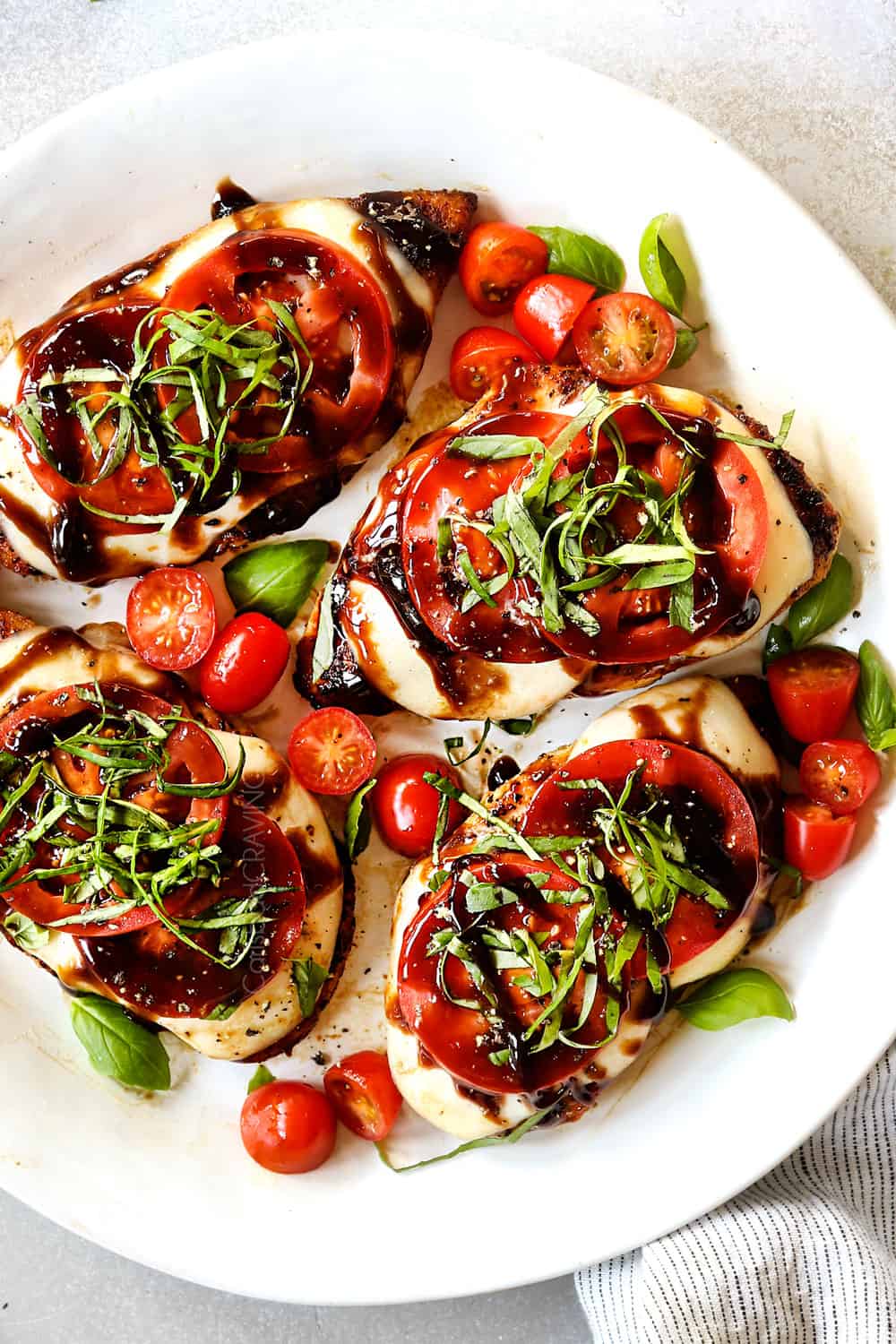 showing how to serve chicken Caprese recipe by adding chicken to a serving platter and drizzling with balsamic glaze