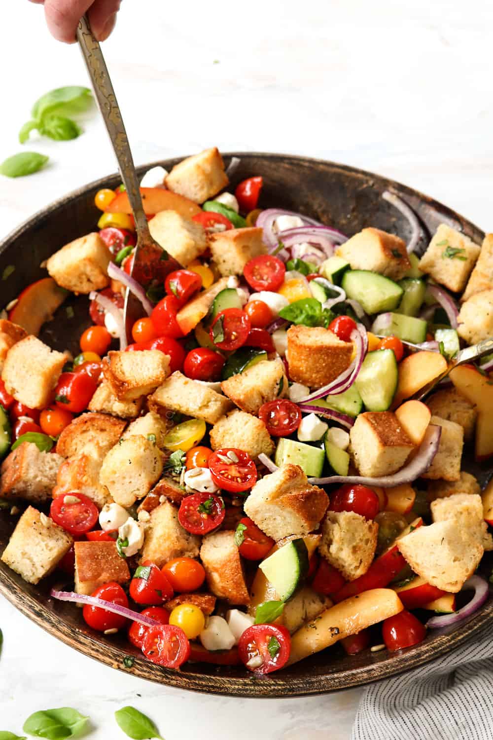 showing how to make Panzanella by tossing the bread, tomatoes and dressing in a wooden bowl