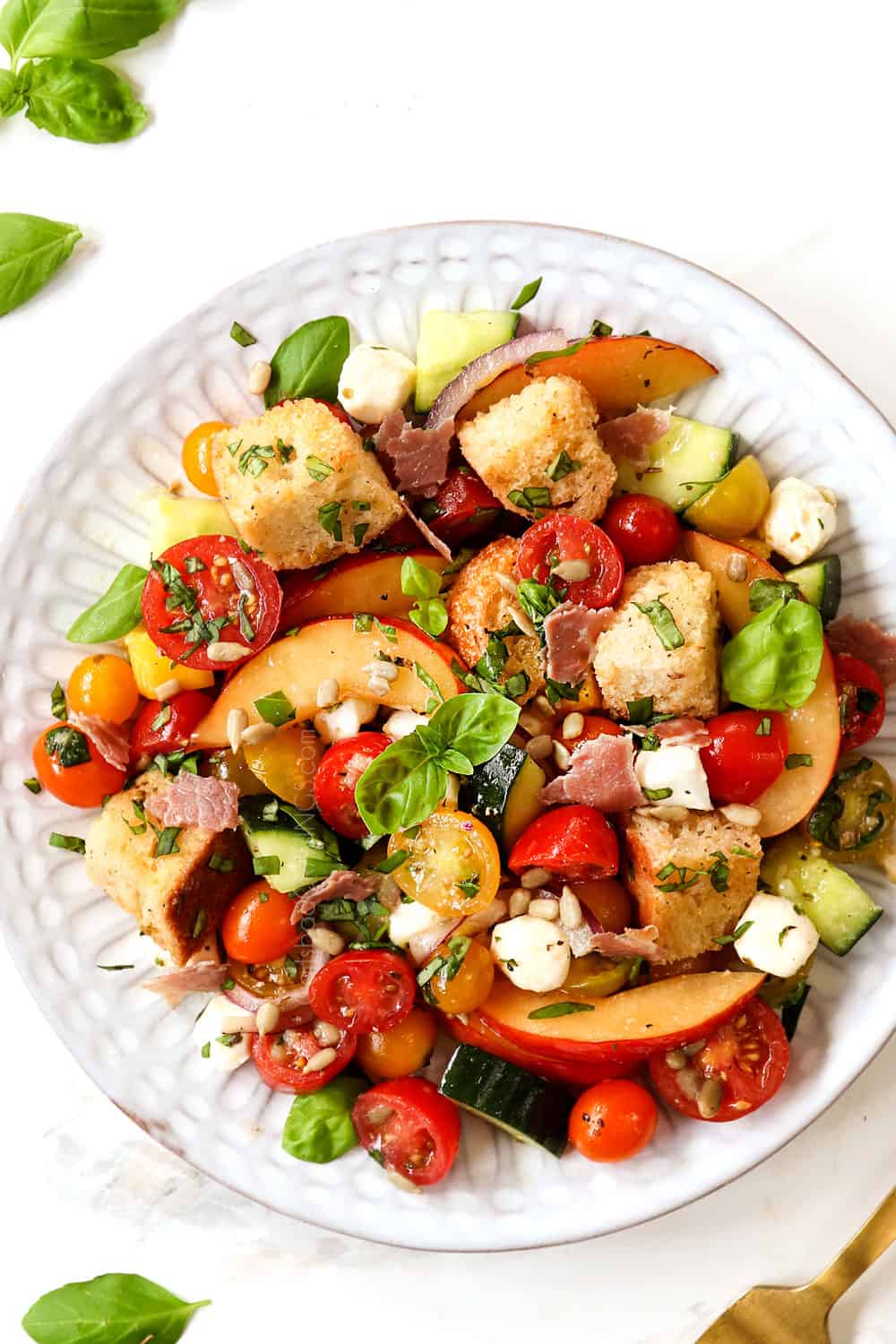 Panzanella salad on a white serving plate garnished with salt and pepper, soaked in red wine vinaigrette