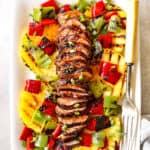 top view of marinated pork tenderloin sliced on a white platter with pineapple, and bell peppers