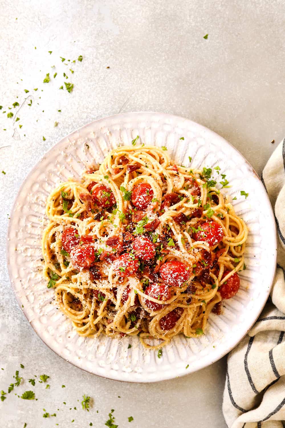 top view of bacon pasta with tomatoes, garlic and Parmesan on a white plate