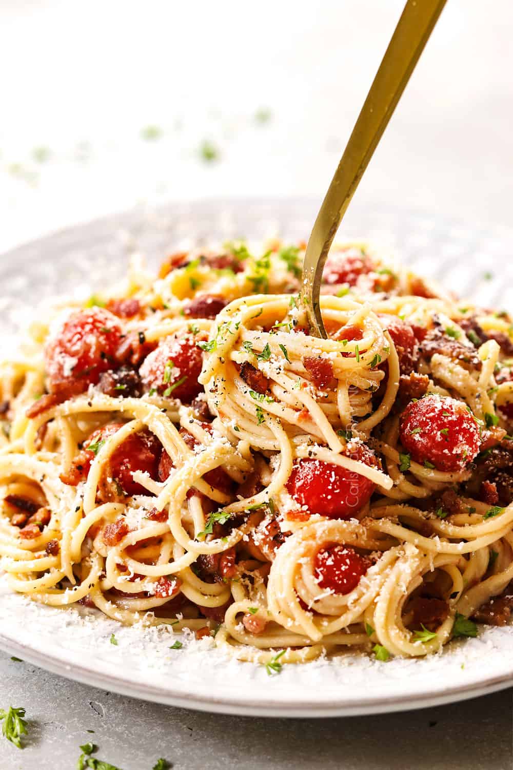 up close of a fork twirling tomato bacon pasta on a white plate