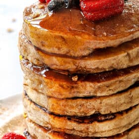 showing how to serve cereal pancakes by pouring syrup over a stack of pancakes