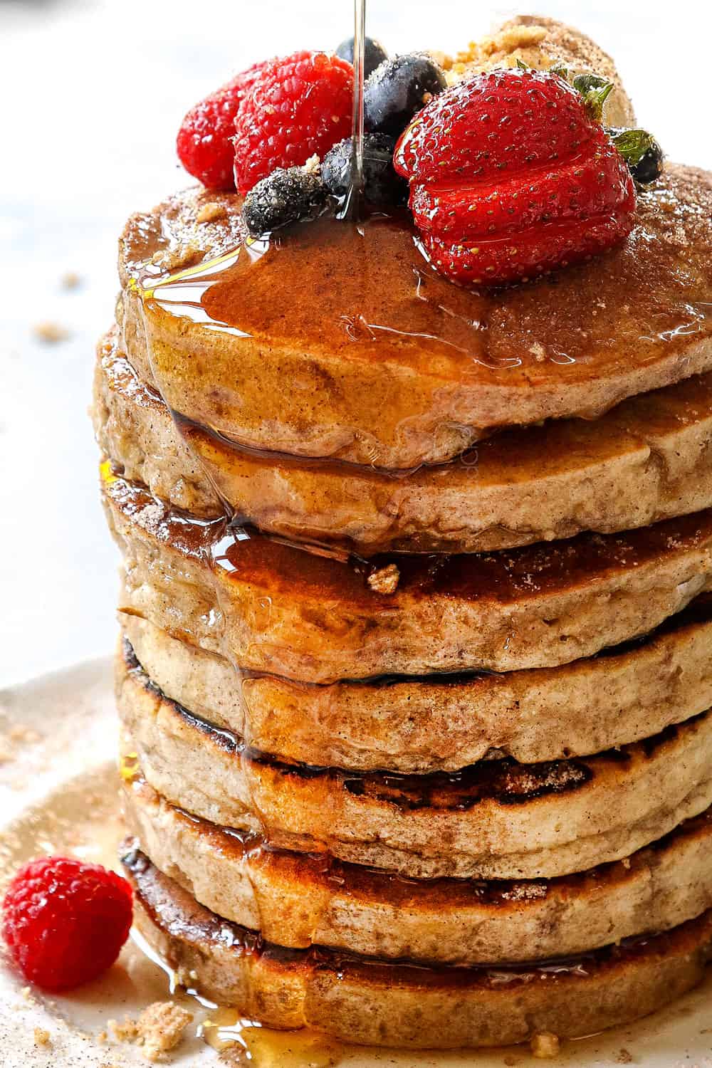 showing how to serve cereal pancakes by pouring syrup over a stack of pancakes