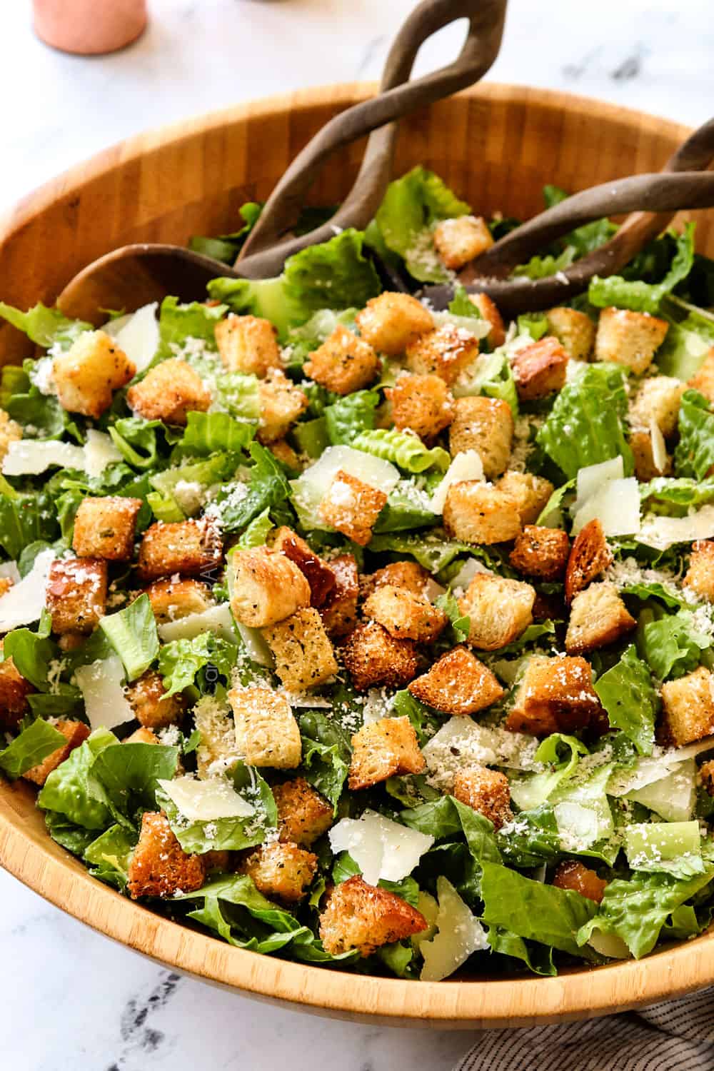 showing what's in Caesar Salad recipe by adding Romaine lettuce, croutons, Parmesan and homemade Caesar Dressing to a bowl