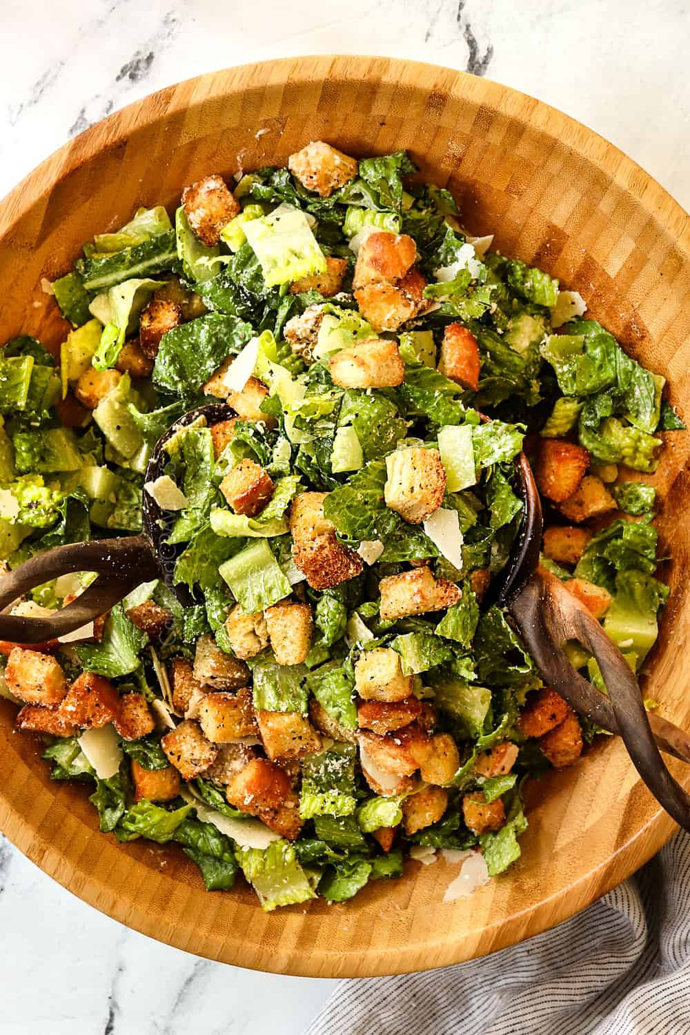 showing how to make Caesar Salad recipe by tossing the salad ingredients together in a wood bowl with tongs