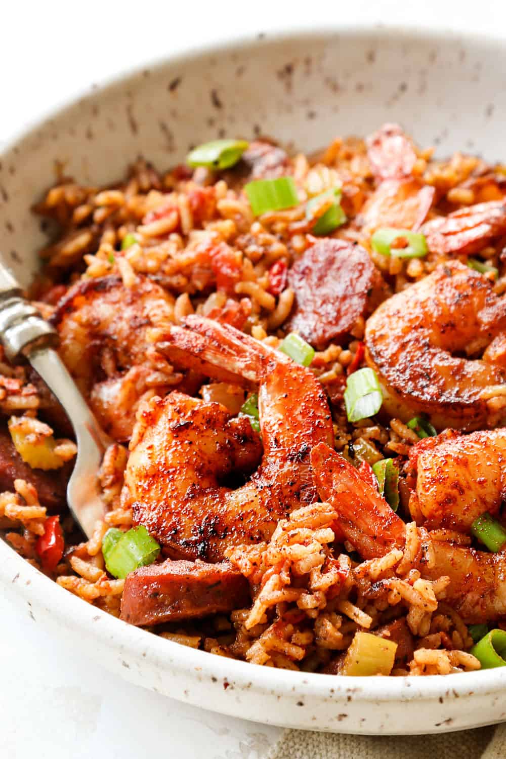 showing how to serve Cajun Shrimp and Rice by adding a serving to a bowl and garnishing with green onions
