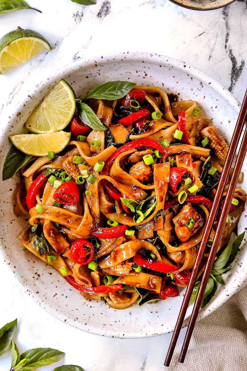 showing how to make Drunken Noodles (Pad Kee Mao) recipe by adding to a white bowl and garnishing with green onions and lime