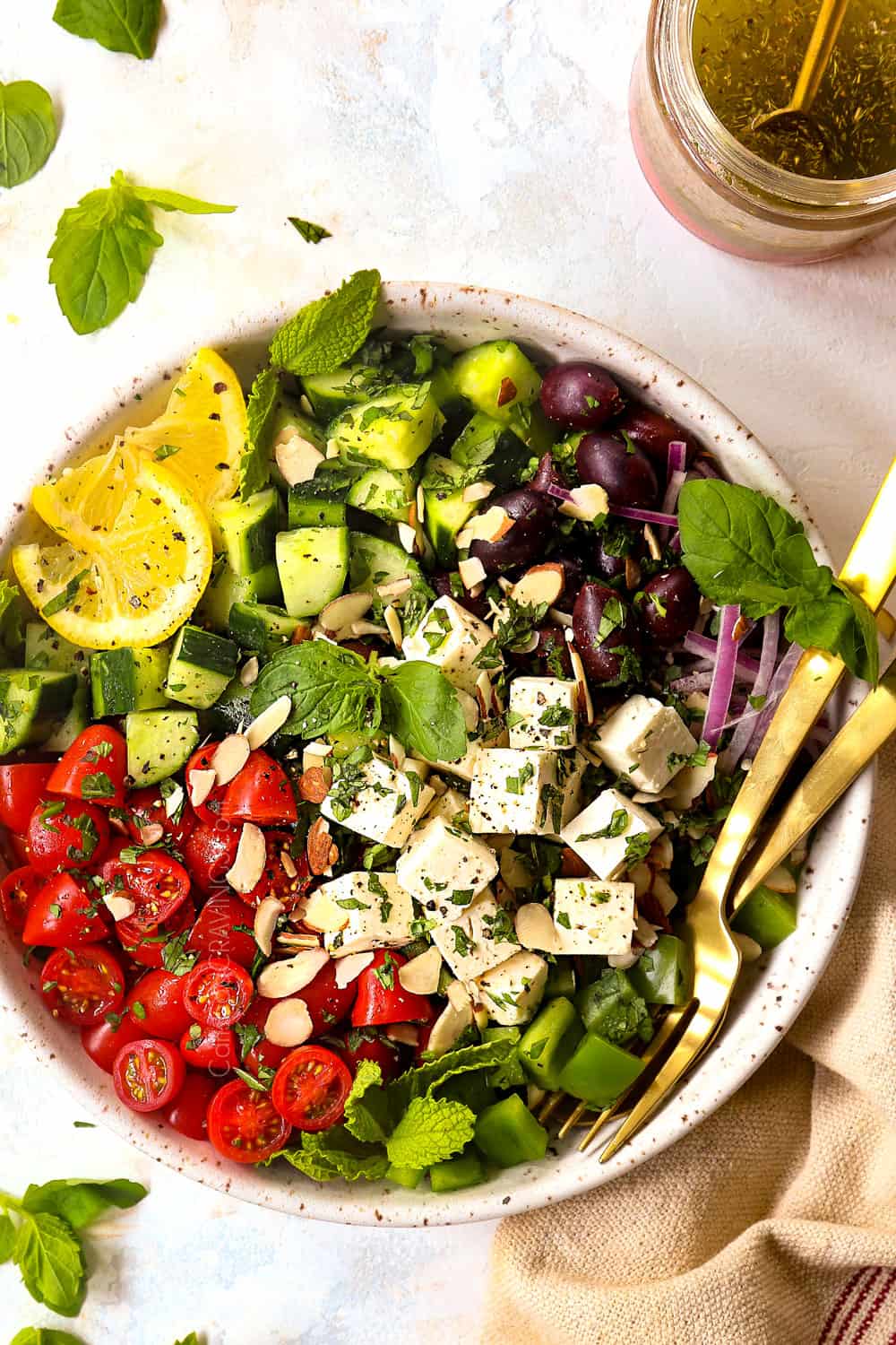 showing how to make Greek Salad by adding tomatoes, Kalamata olives, bell peppers, and feta to a bowl