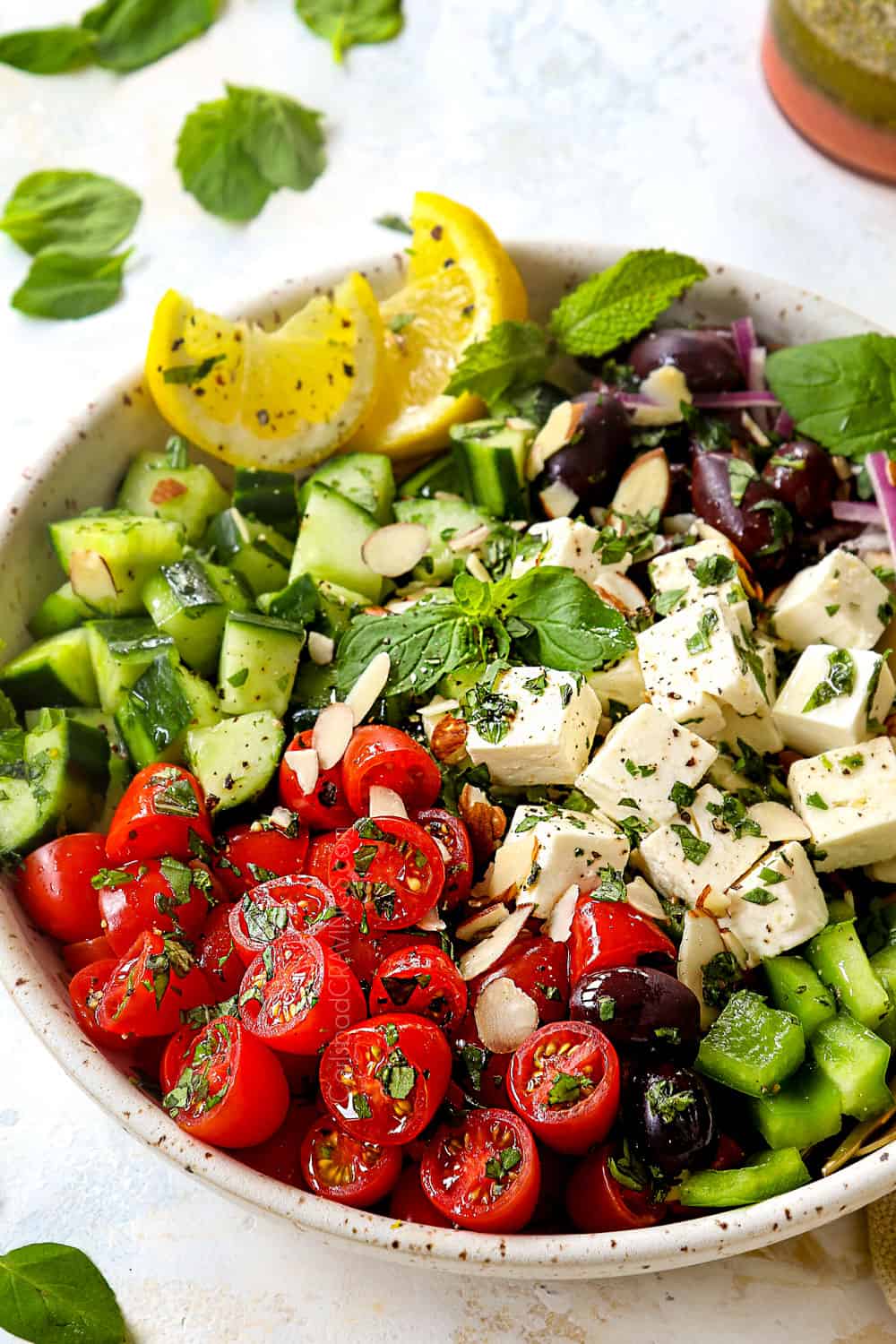 showing how to make Greek Salad by adding Greek Salad ingredients to a bowl: tomatoes, bell peppers, feta, cucumbers, red onions and Kalamata olives