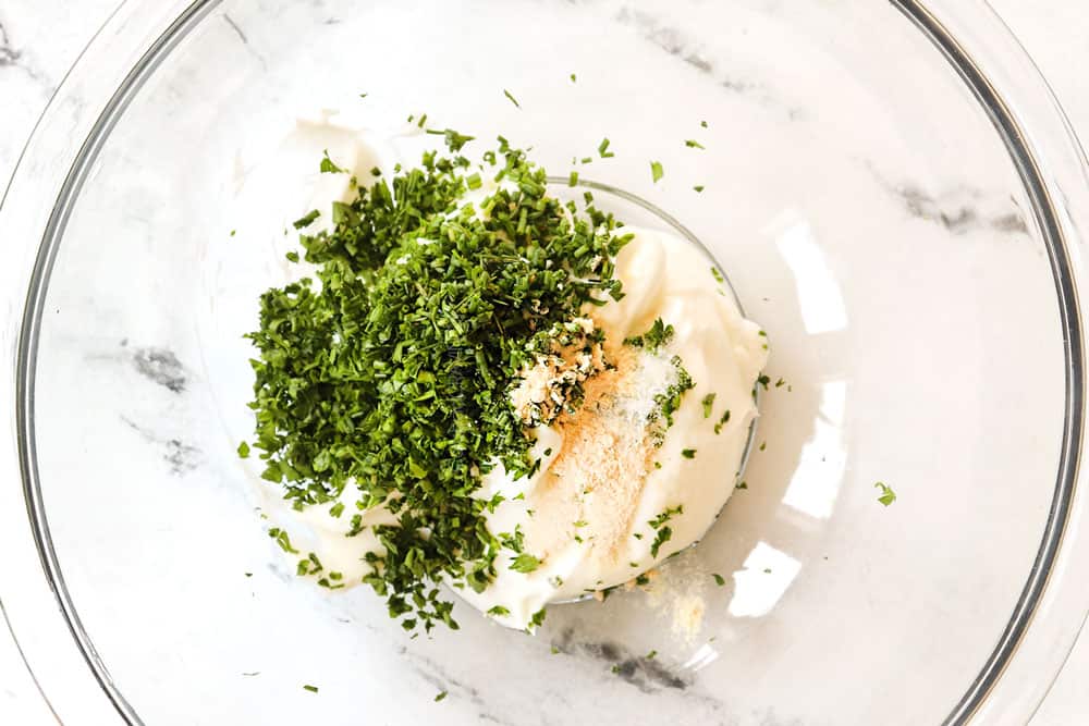 showing how to make lemon garlic chicken recipe by whisking yogurt, chives, parsley and lemon juice together in a glass bowl to make a sauce