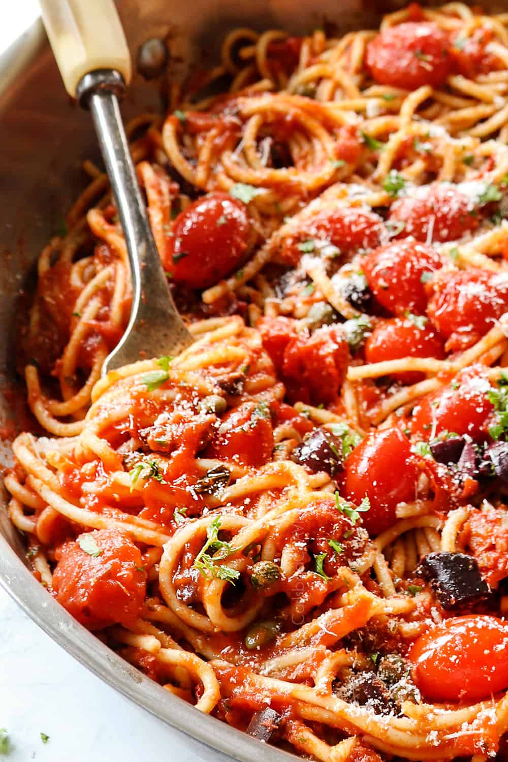 up close of a skillet of Pasta Puttanesca with capers, olives, anchovies, parsley and Parmesan